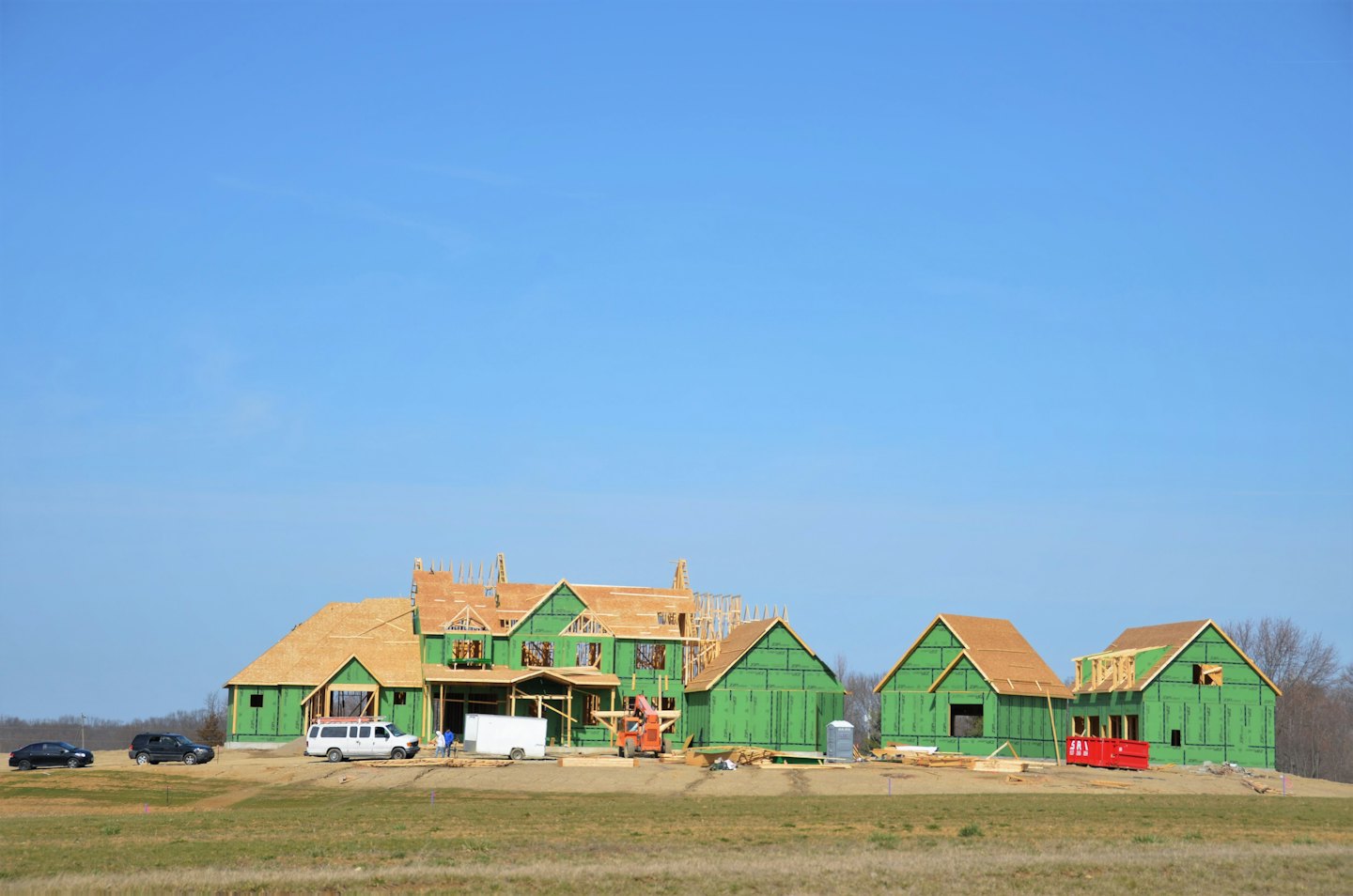 Houses under construction with wooden roofs stand in an open field.