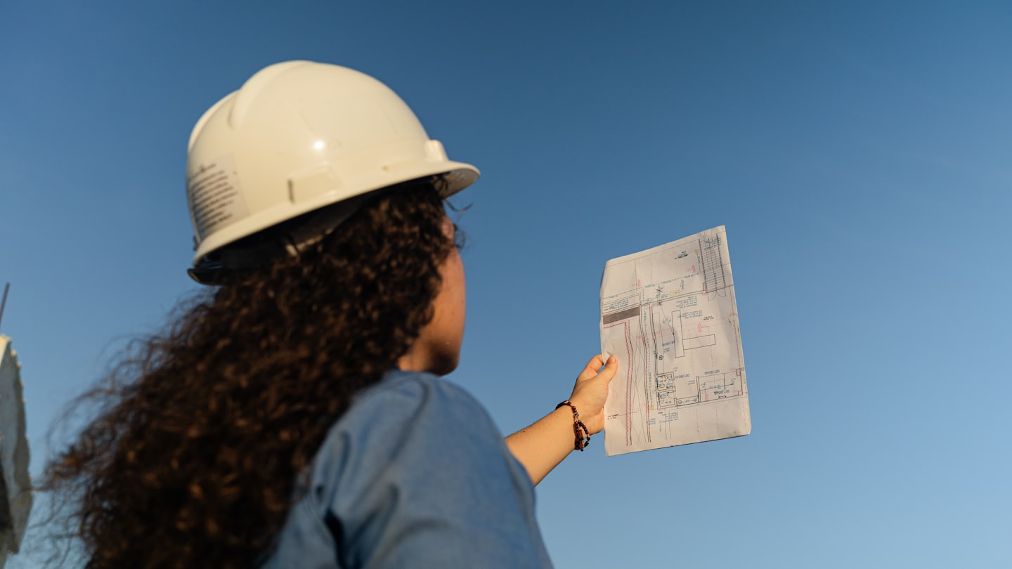 Engineer reviews architectural plans against blue sky.
