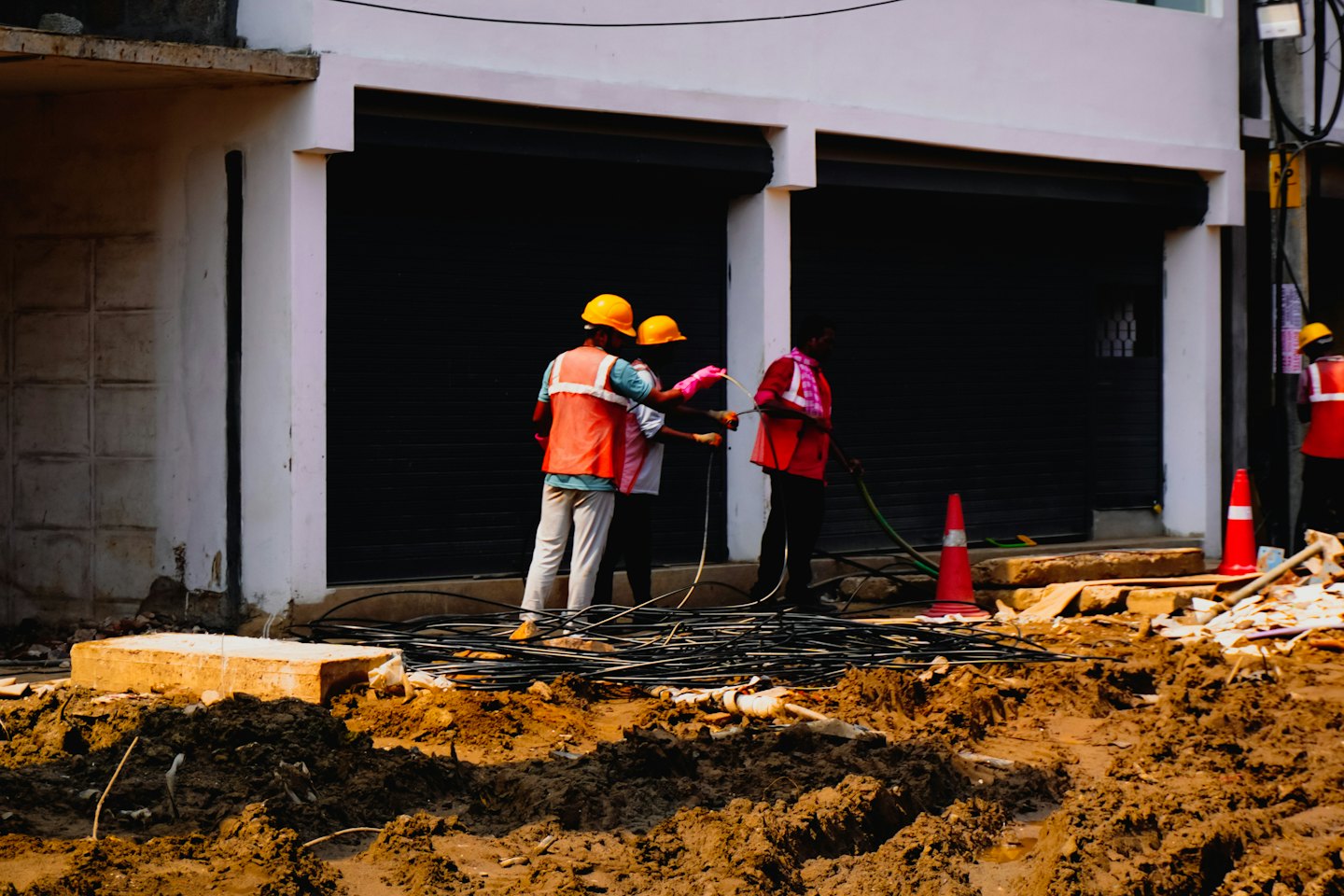 Three utility workers manage electrical cables at a construction site.